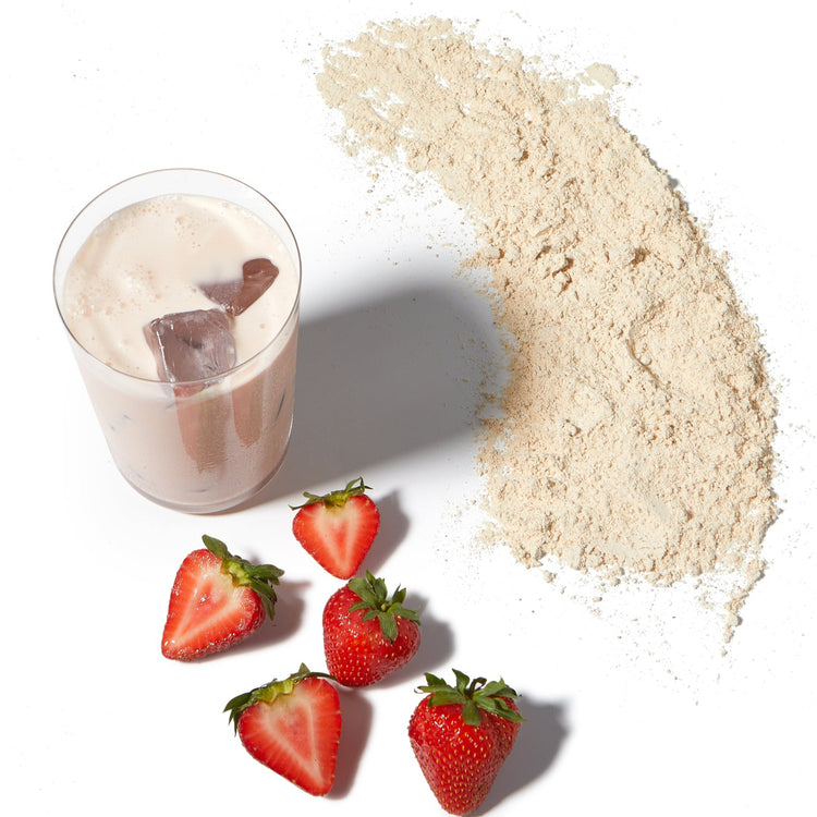 Glass of milkshake with ice cubes, strawberries, and a pile of protein powder on a white background