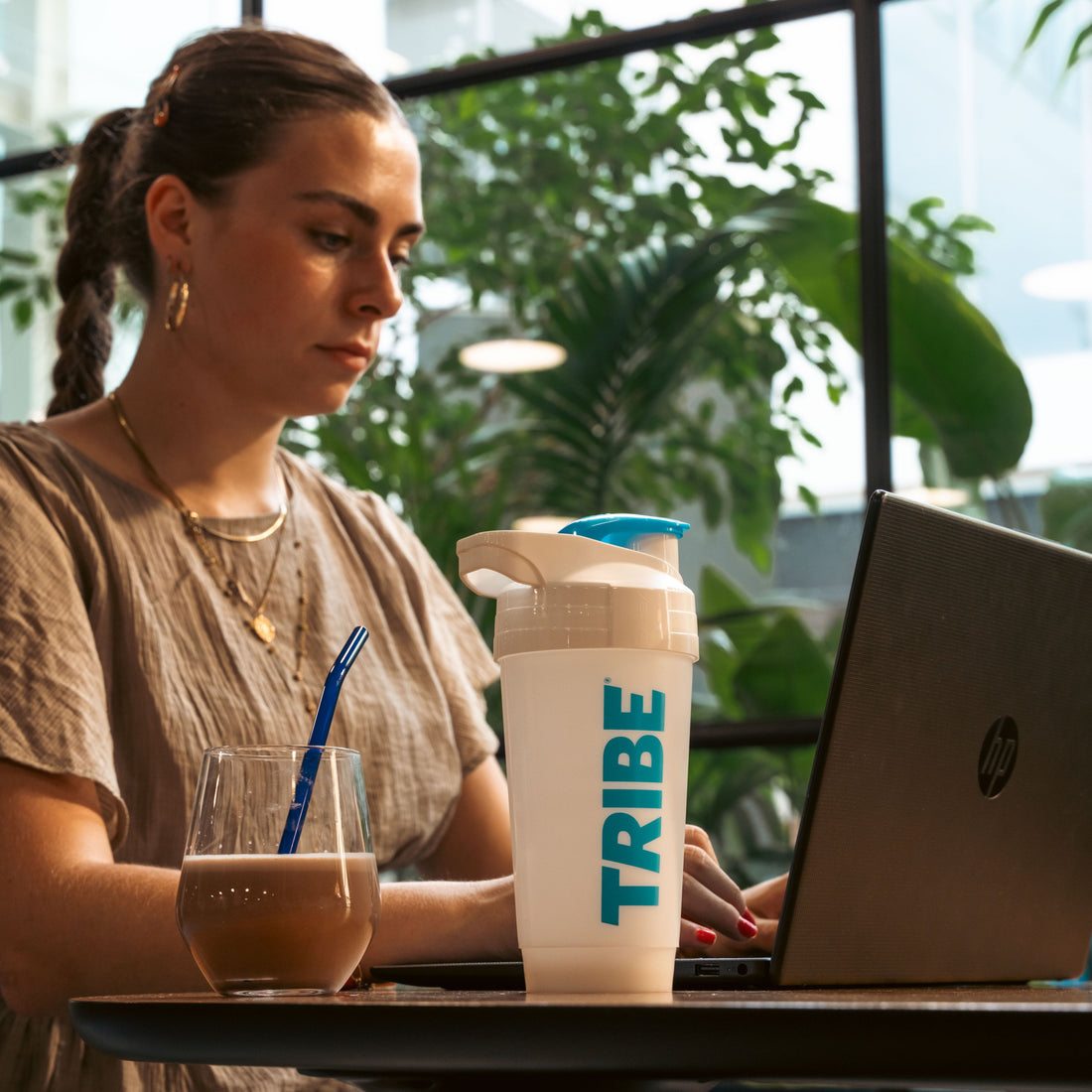 Woman working on a laptop with a 'TRIBE' cup in a modern office setting