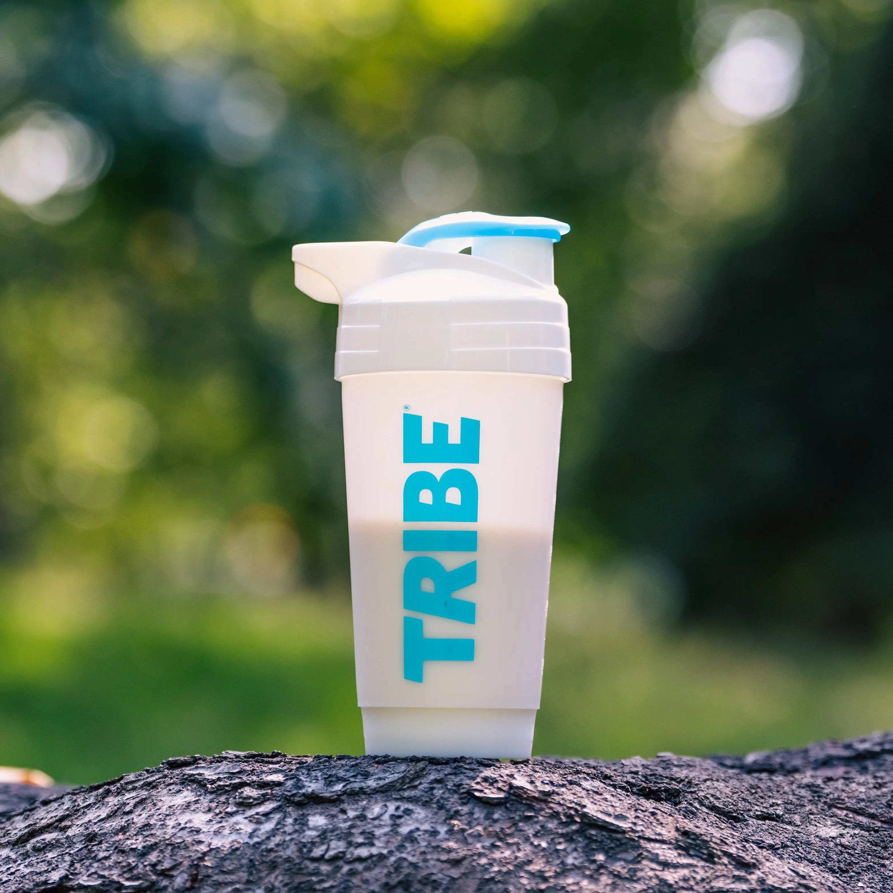 Shaker cup with 'TRIBE' branding on a tree stump outdoors